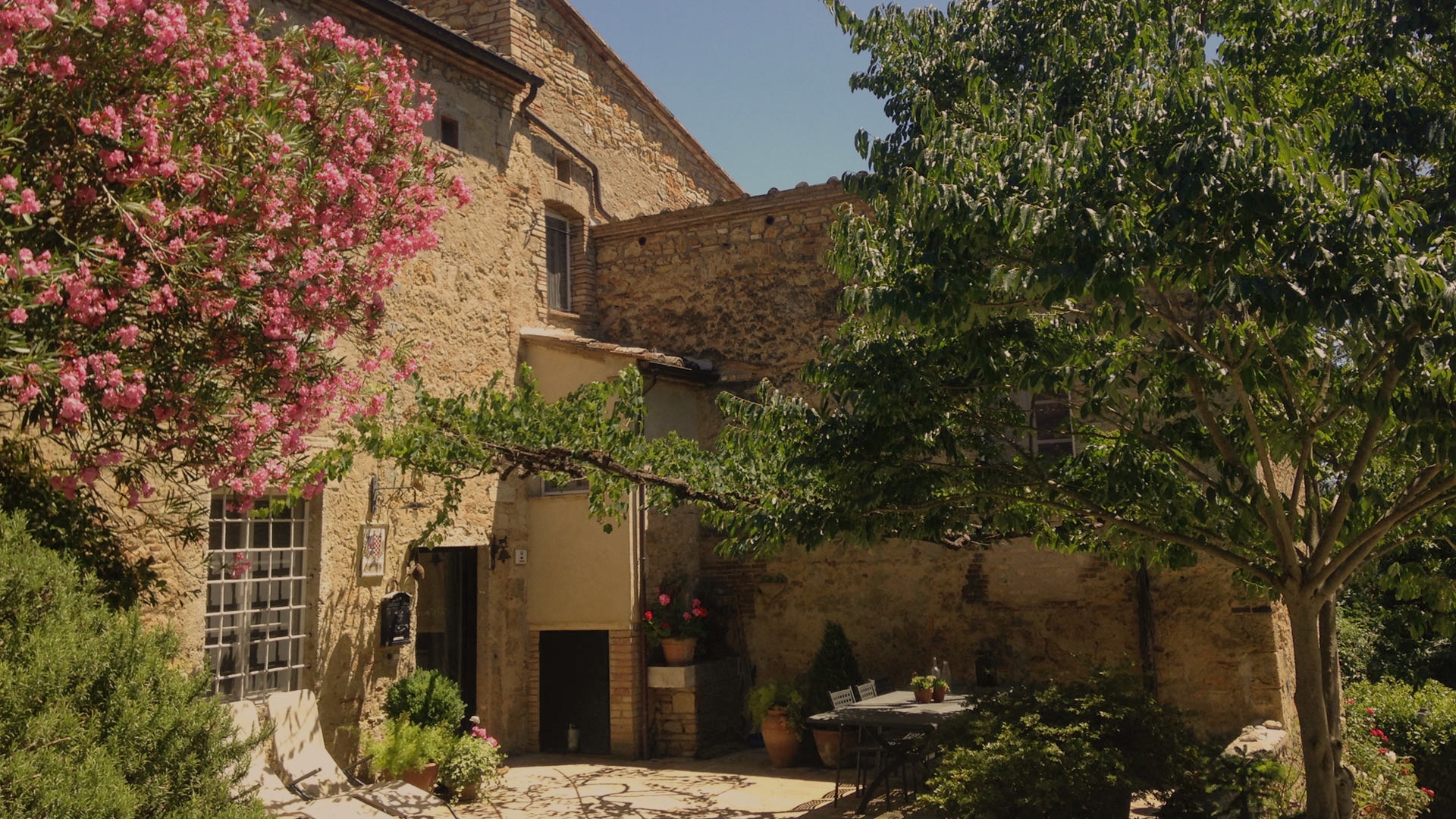 Il casale in pietra della tenuta, con l'oleandro in fiore e la corte